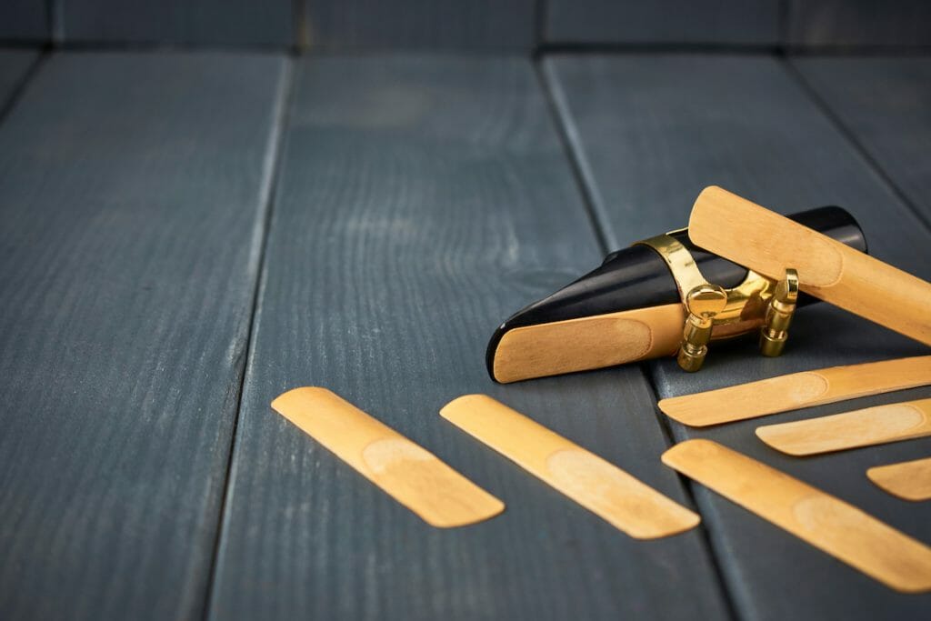 saxophone mouthpiece and reed with clamp and gold hardware along with replacement reeds on gray wooden background